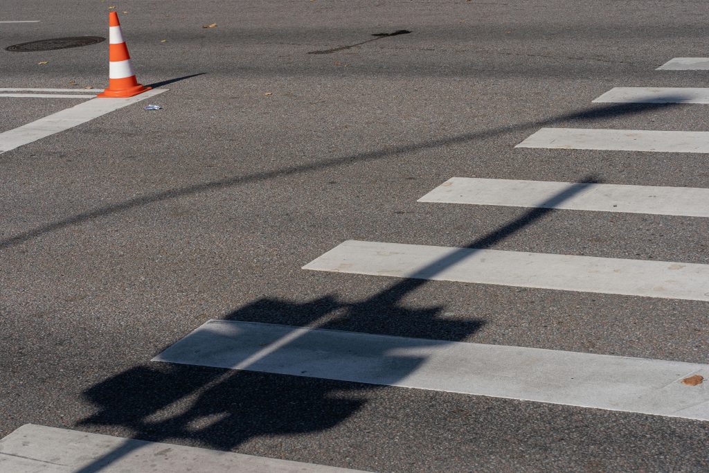 Street scene with a traffic cone, crosswalk, and shadows, capturing urban infrastructure.